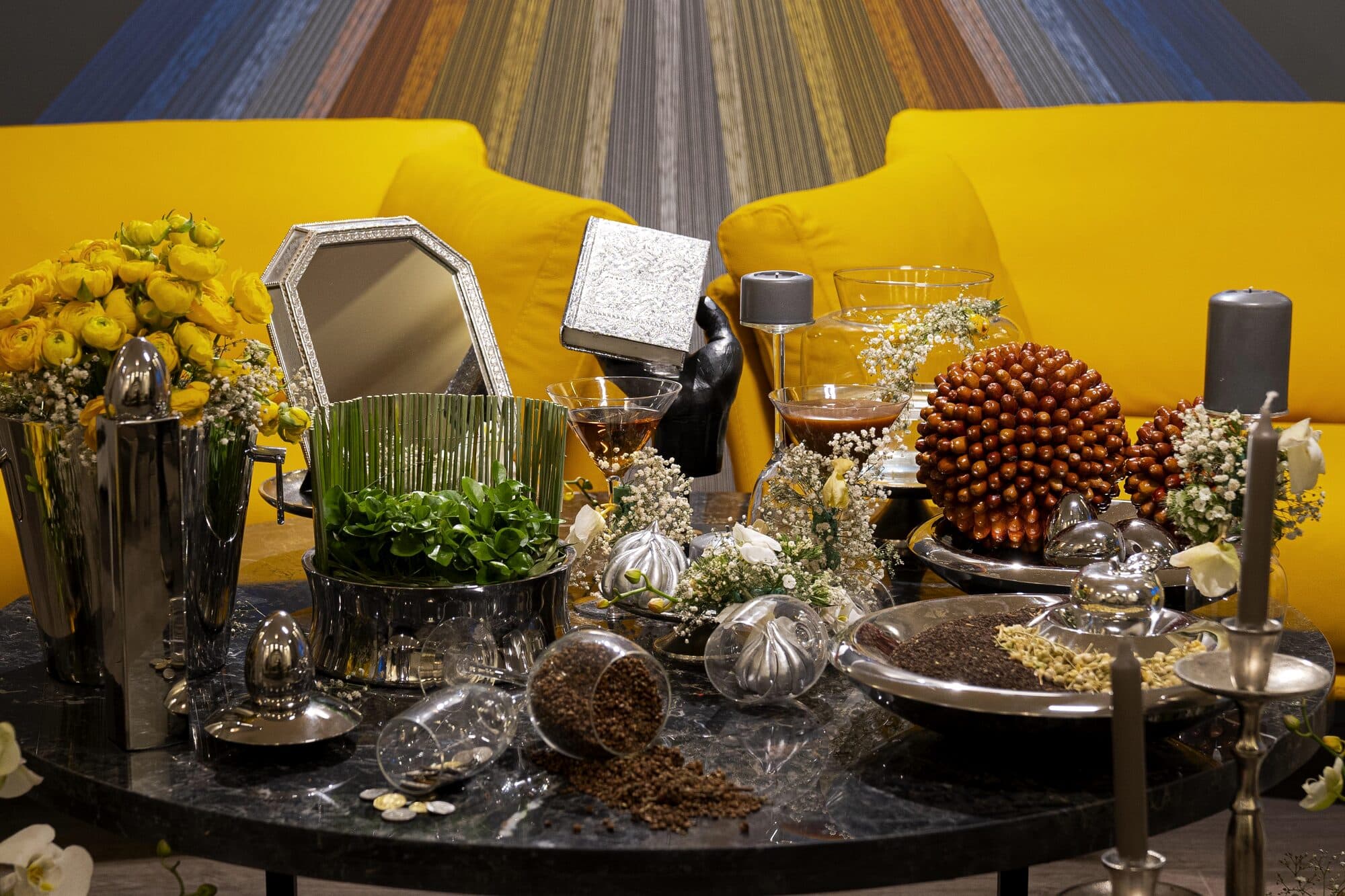 The evening's set with nobody in it: a woven thread backdrop, the yellow sofa, and the Haft-Seen laid out on dark marble.