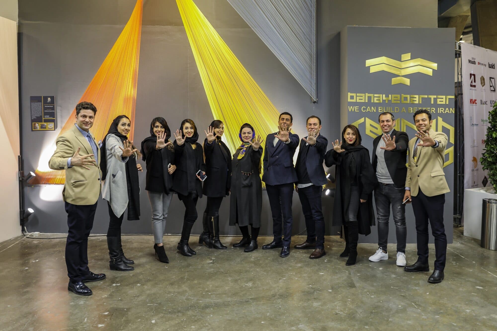 The team on the floor at WINDOW DISPLAY Tehran, hands raised, in front of the thread installation and the Banaye Bartar signage wall