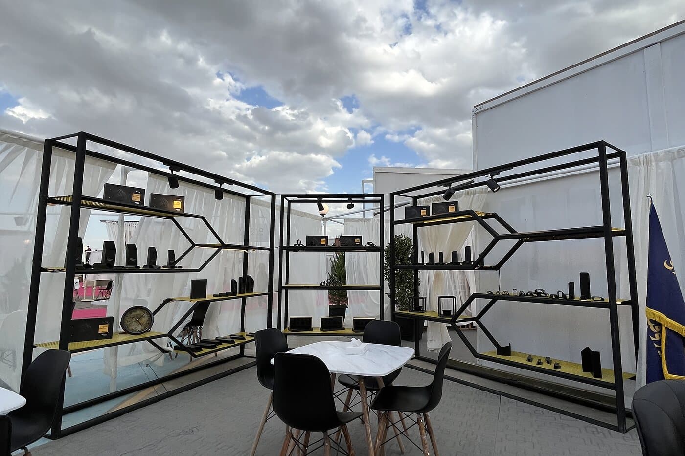 A black steel lattice pavilion open to the sky, its shelves reading as a structure before they read as a display